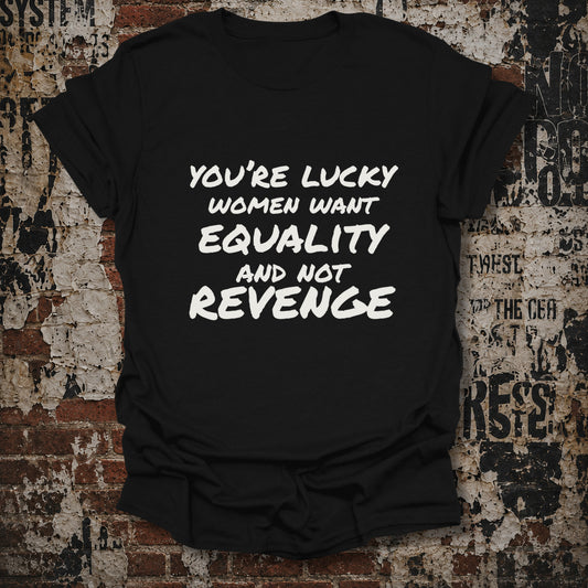 A black short-sleeve graphic T-shirt laid flat against a distressed brick and concrete wall. The shirt has bold white text reading, 'YOU'RE LUCKY WOMEN WANT EQUALITY AND NOT REVENGE.
