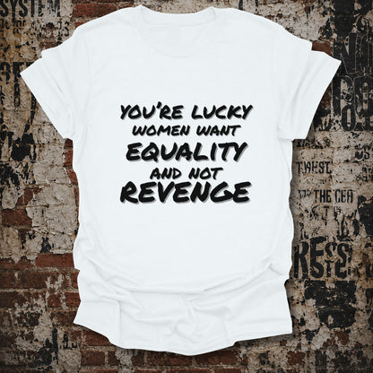 A white short-sleeve graphic t-shirt with black text reading 'YOU'RE LUCKY WOMEN WANT EQUALITY AND NOT REVENGE', displayed flat against a distressed, textured brick wall background.