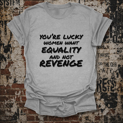 A light gray heather t-shirt with black text reading 'YOU'RE LUCKY WOMEN WANT EQUALITY AND NOT REVENGE', displayed flat against a distressed brick wall background.