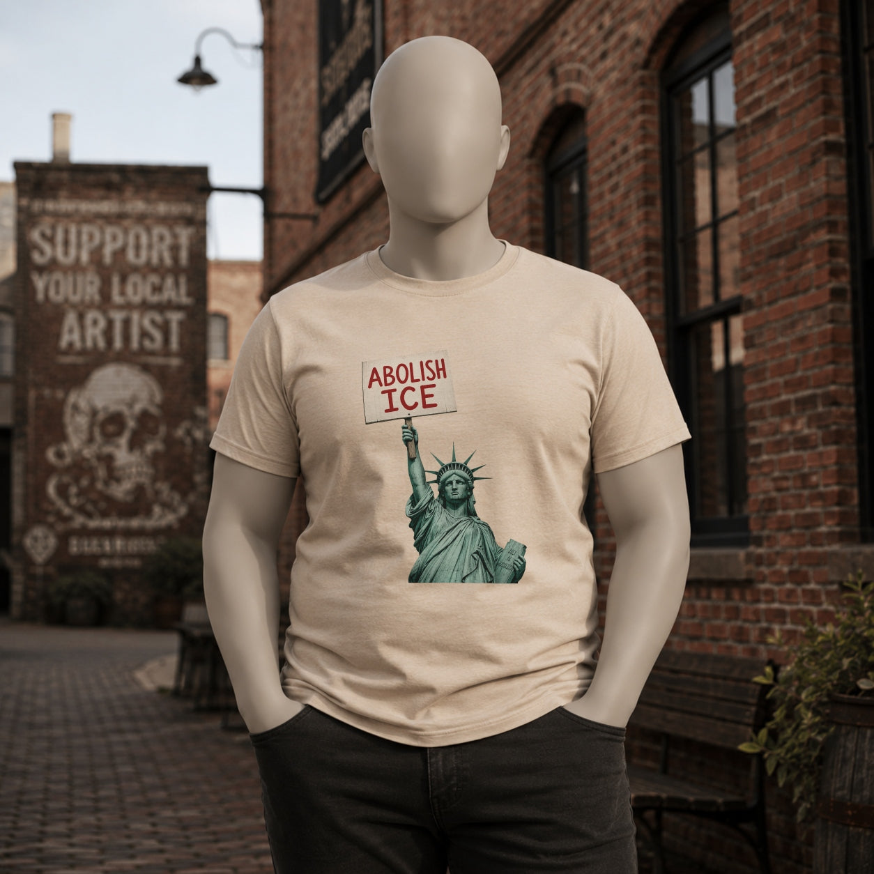 Sand Abolish ICE Statue of Liberty T-shirt on a matte mannequin in an urban brick setting